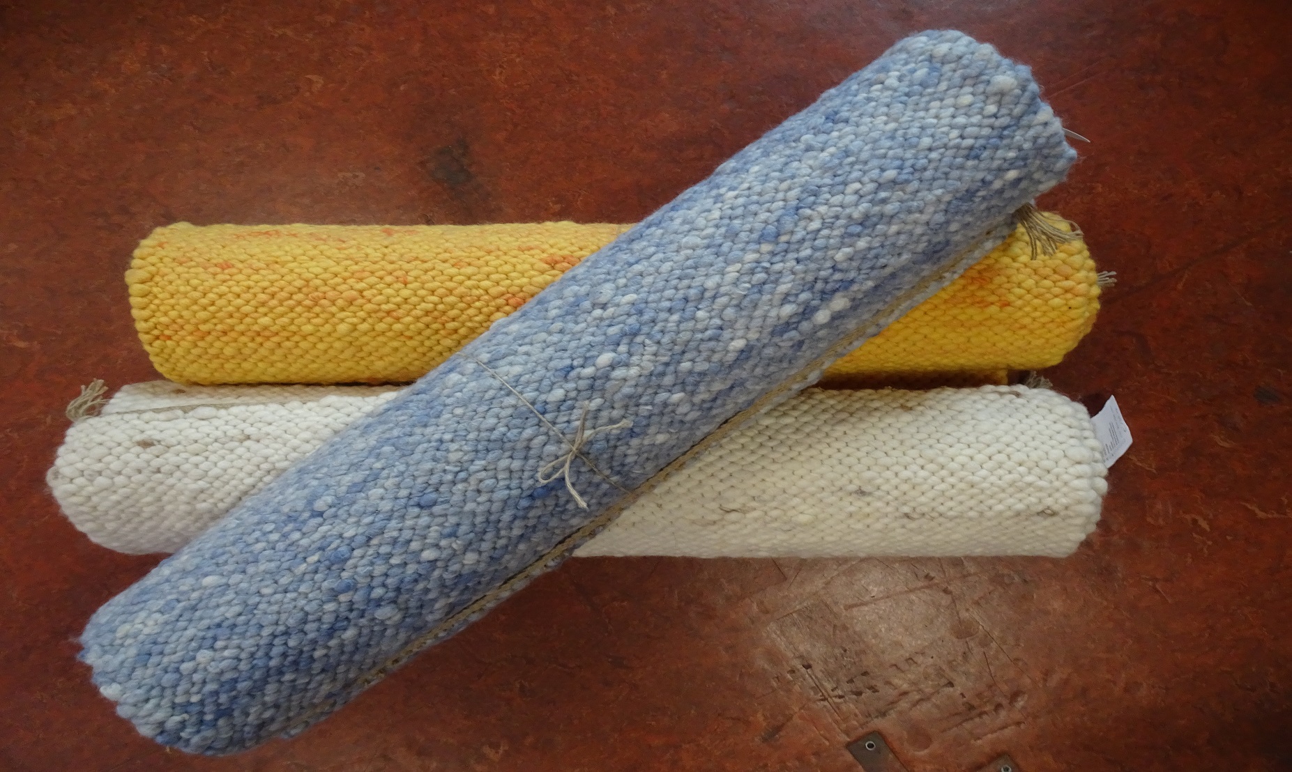 Drei Teppichrollen in gelb, hellblau und natur